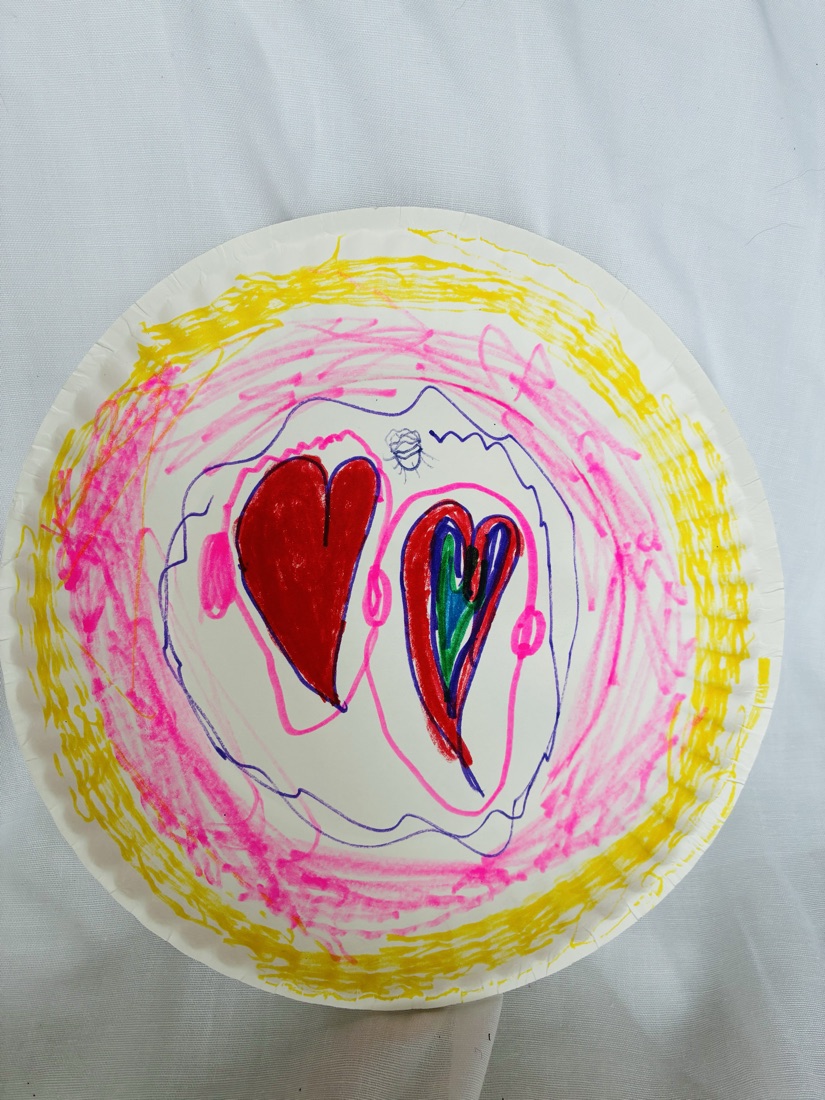 A paper plate decorated with two hearts, one red and one rainbow, surrounded by radiating pink and yellow