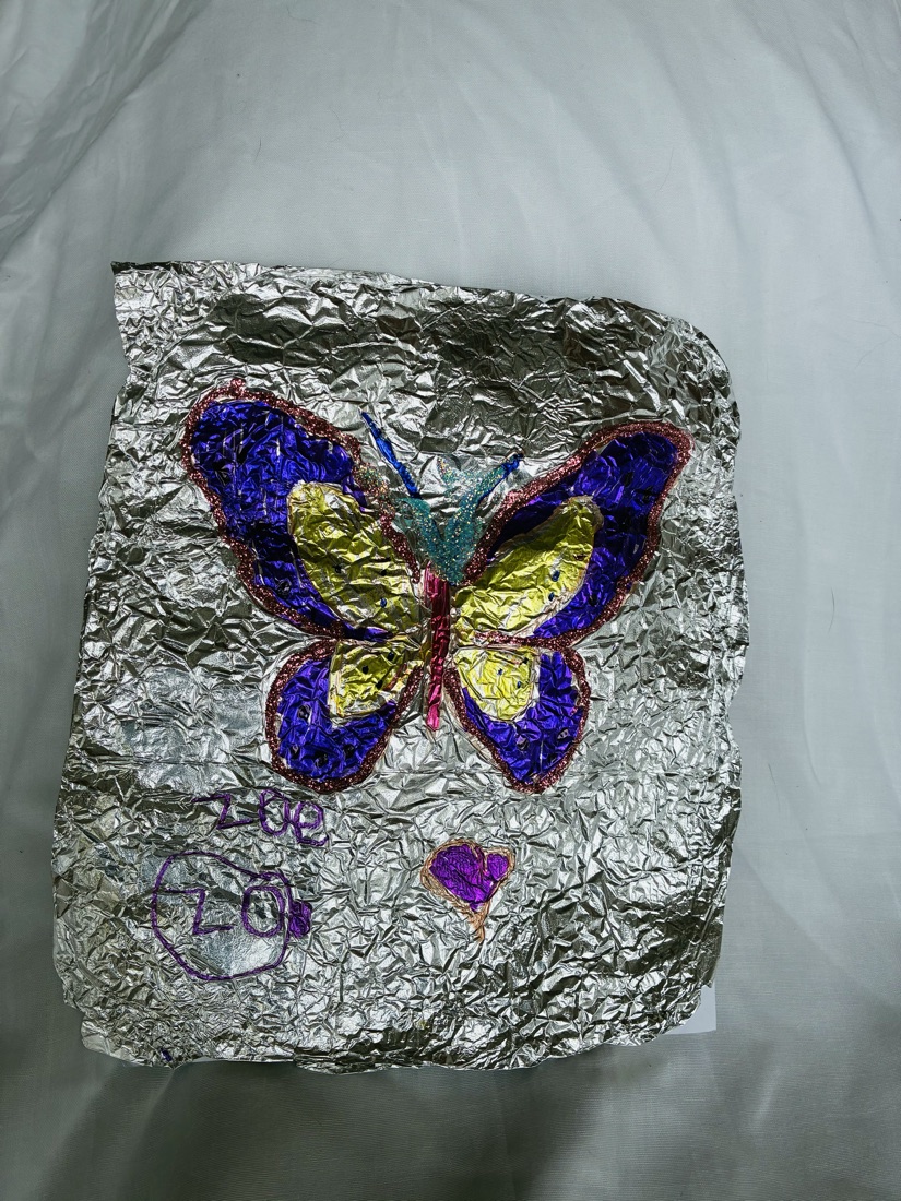 A butterfly with purple and yellow wings drawn on crinkled silver foil, outlined in glitter, signed Zoe 2024