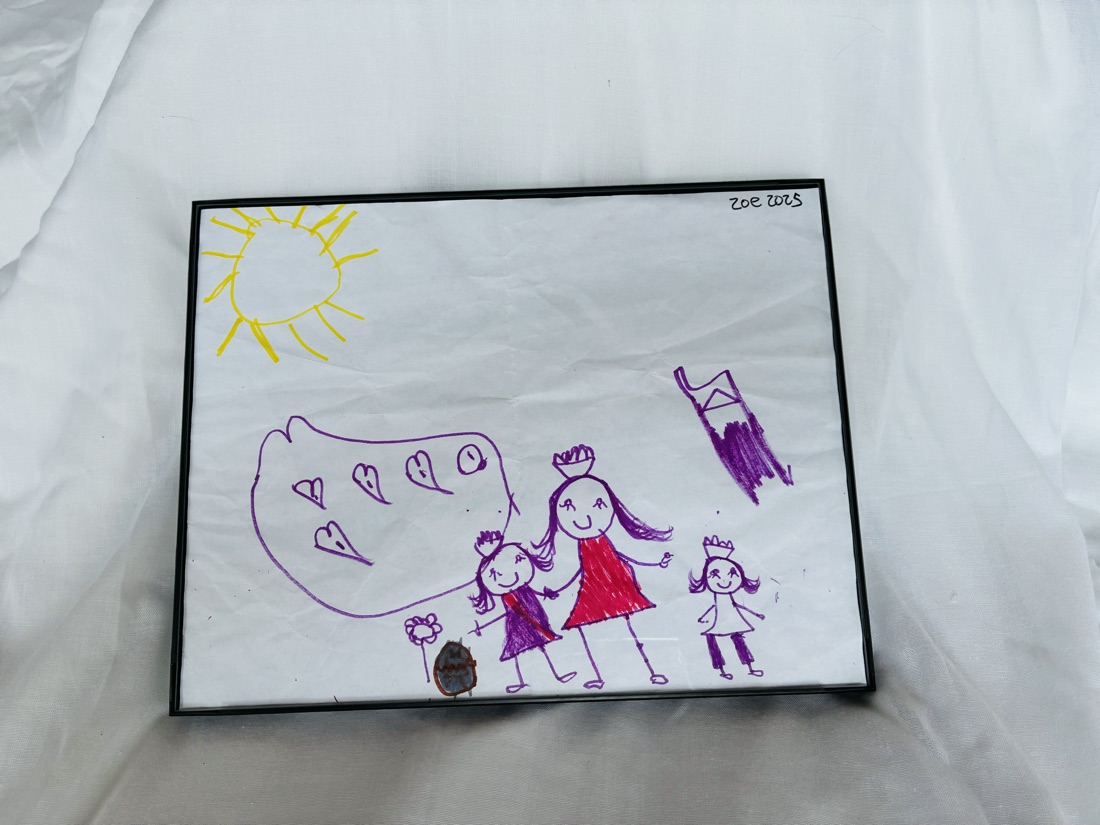 Marker drawing of three smiling figures holding hands beside a purple dragon, with a yellow sun above, signed Zoe 2025